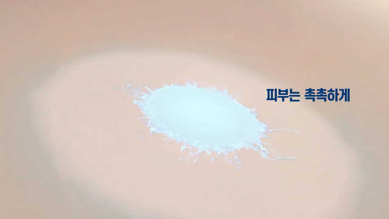 Close-up of a milky lotion splash landing on skin, beside Korean text reading "피부는 촉촉하게" (skin, kept moisturised)