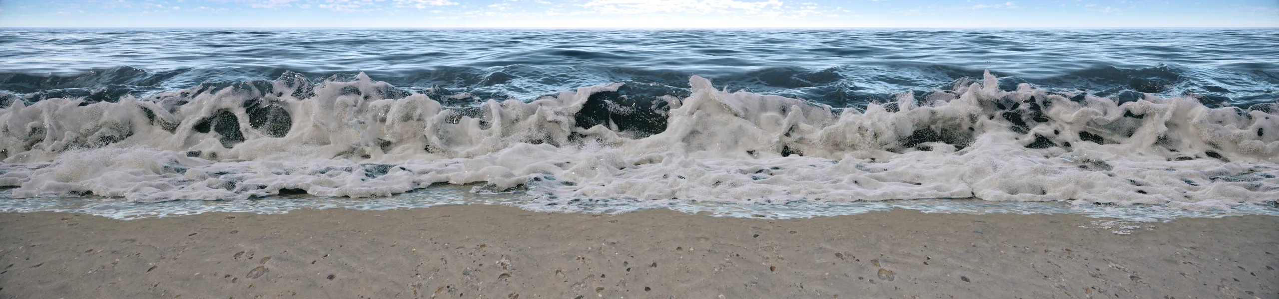 Ocean waves breaking on a shoreline, shown as wide panoramic footage