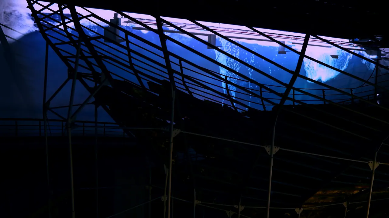Angled projection wall showing wave footage behind a support structure in a darkened exhibition hall