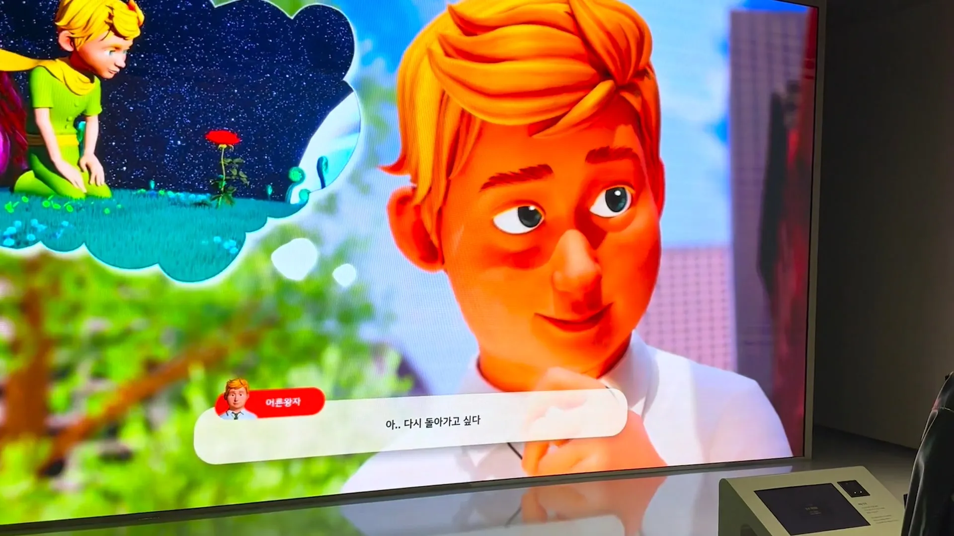 LED wall showing the office-worker character in close-up beside a thought bubble of his younger self as the Little Prince, kneeling by a rose under a starfield